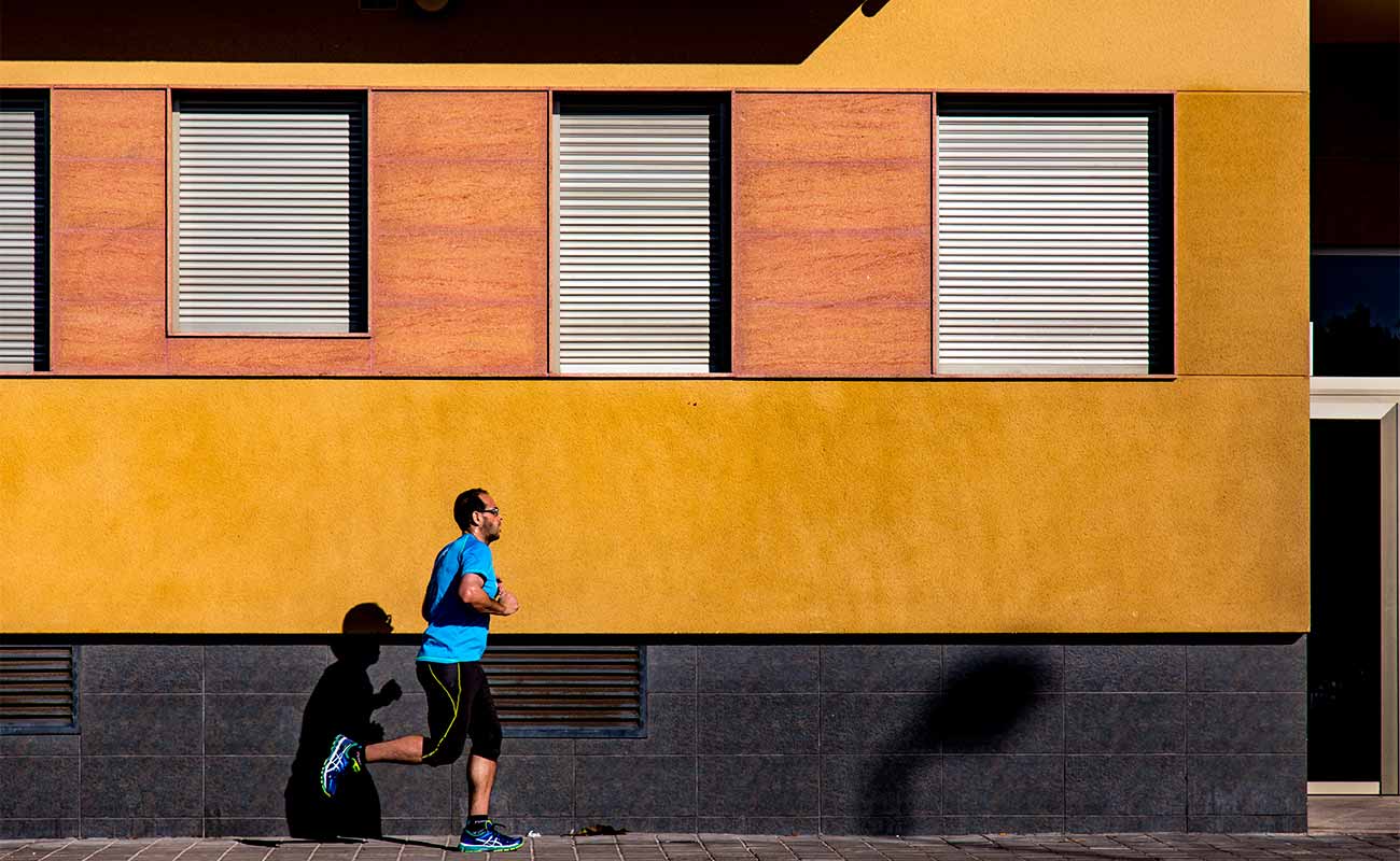 A man jogging in front of a yellow building.