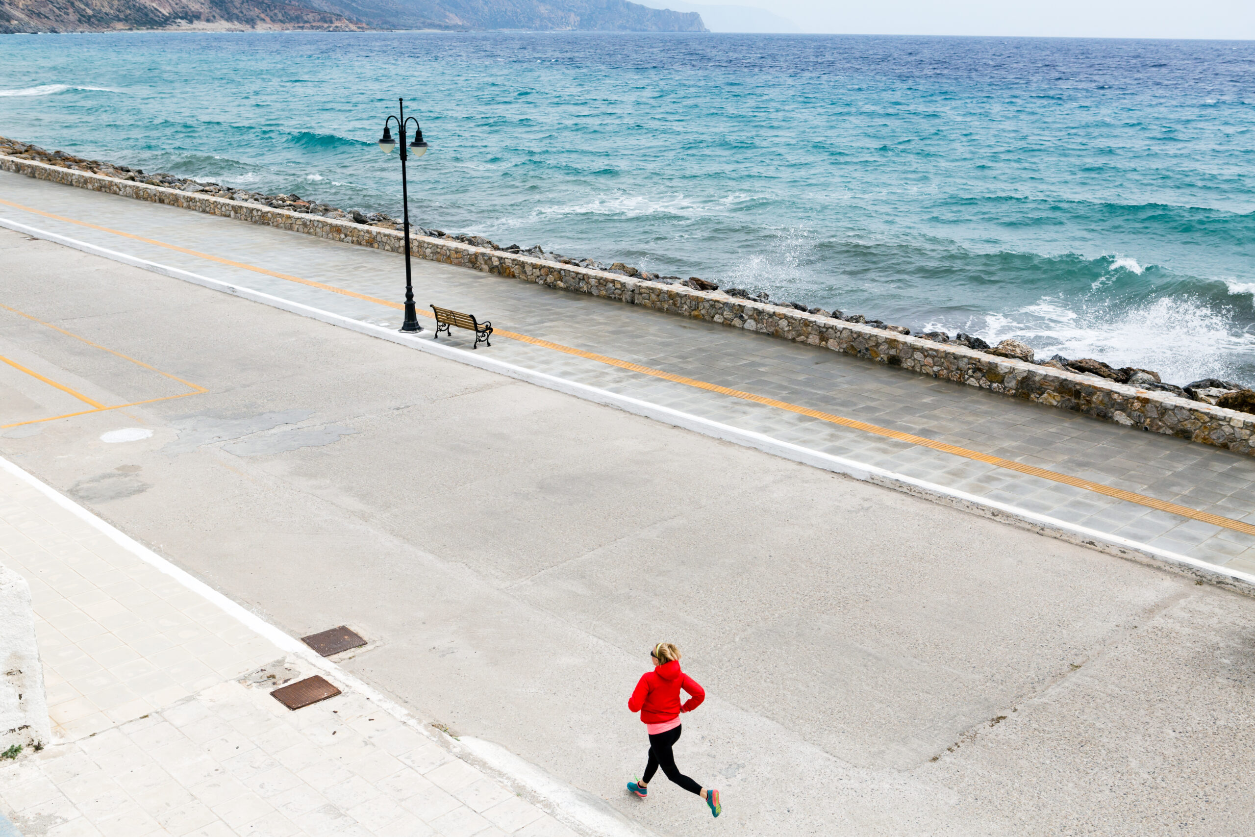 A woman is running down a street next to the ocean during her personal running record in the United States.