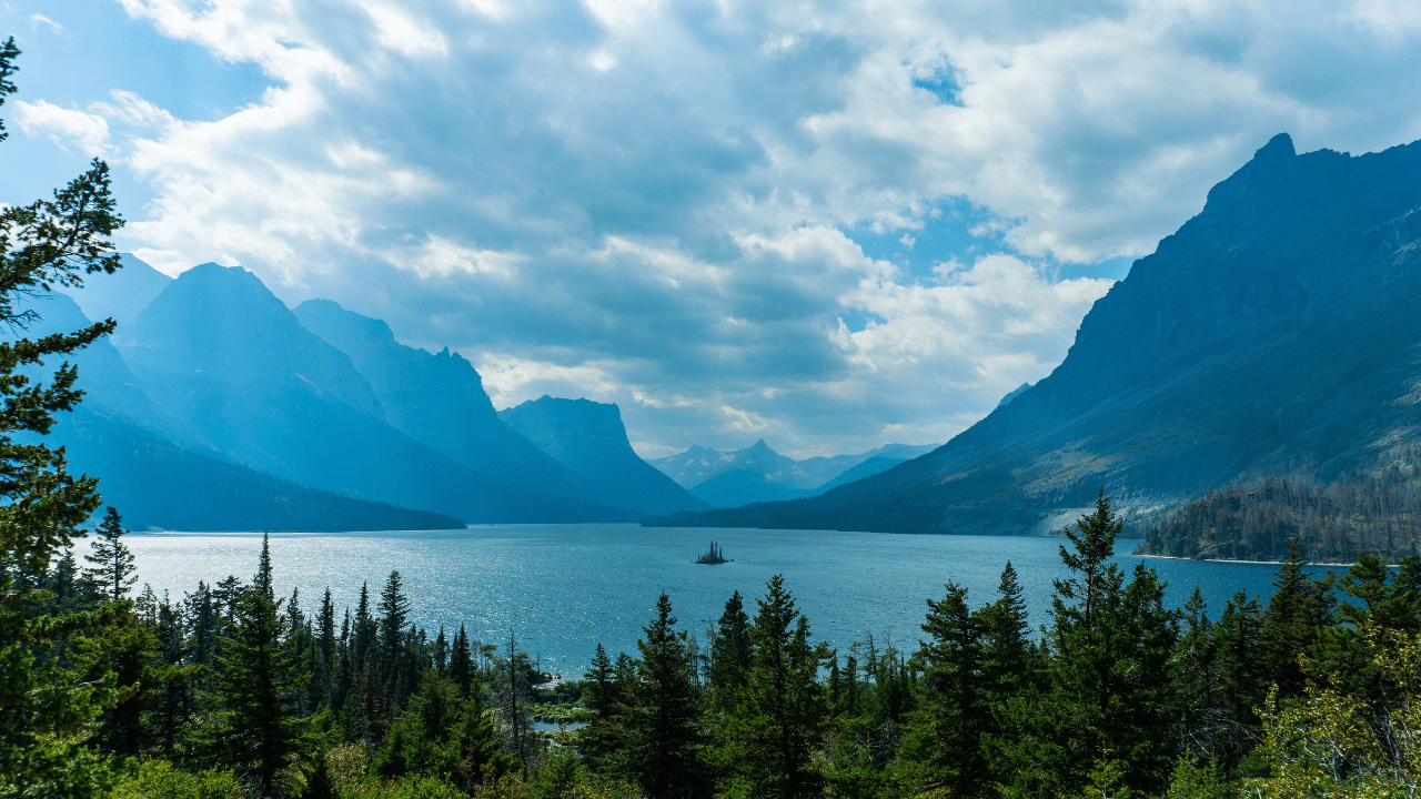 A glacier-fed lake surrounded by towering mountains and lush trees.