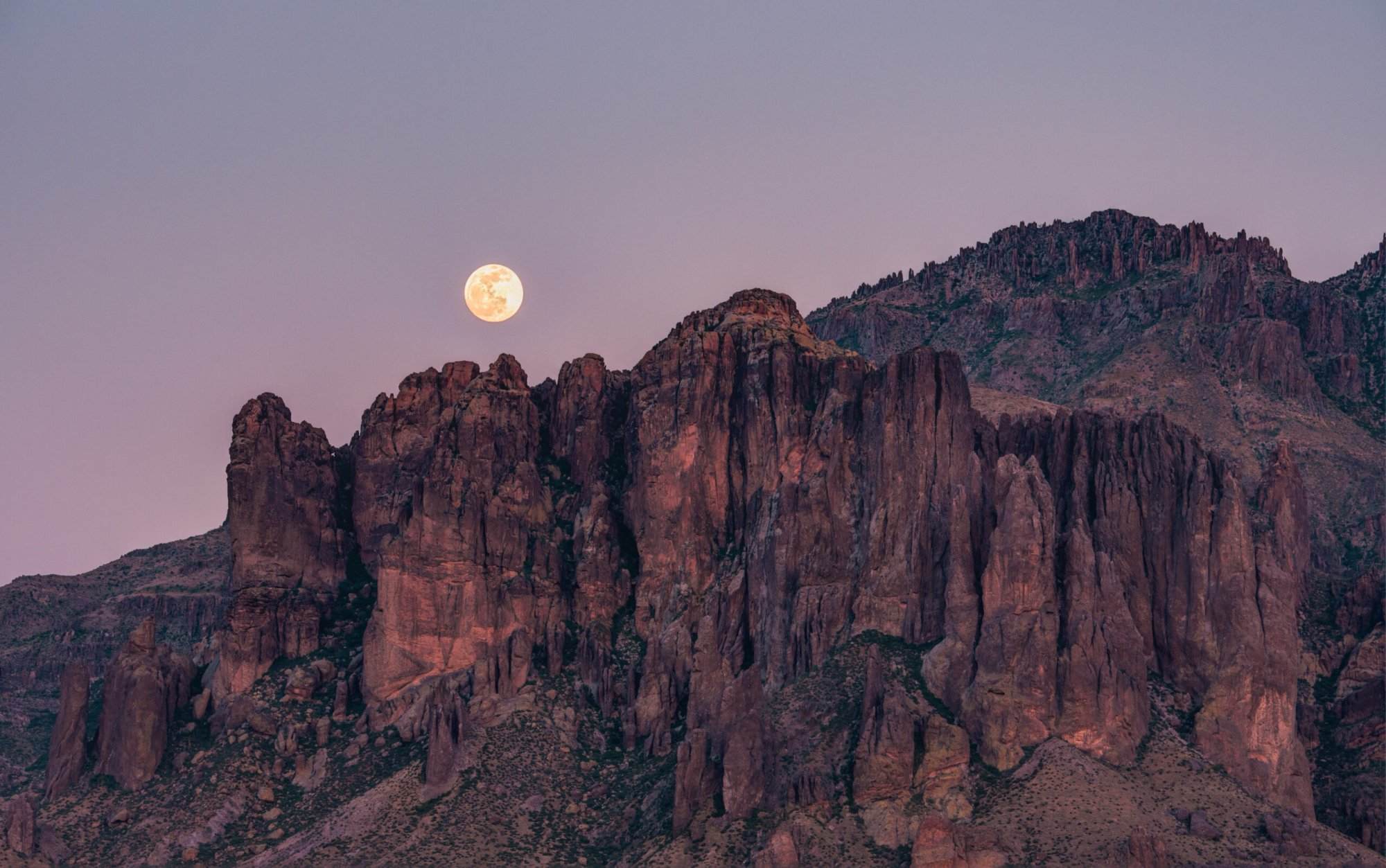 A full moon rises over a mountain range.