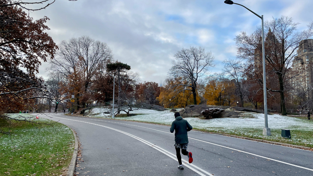 A man, staying motivated, is running down a snowy road in central park.