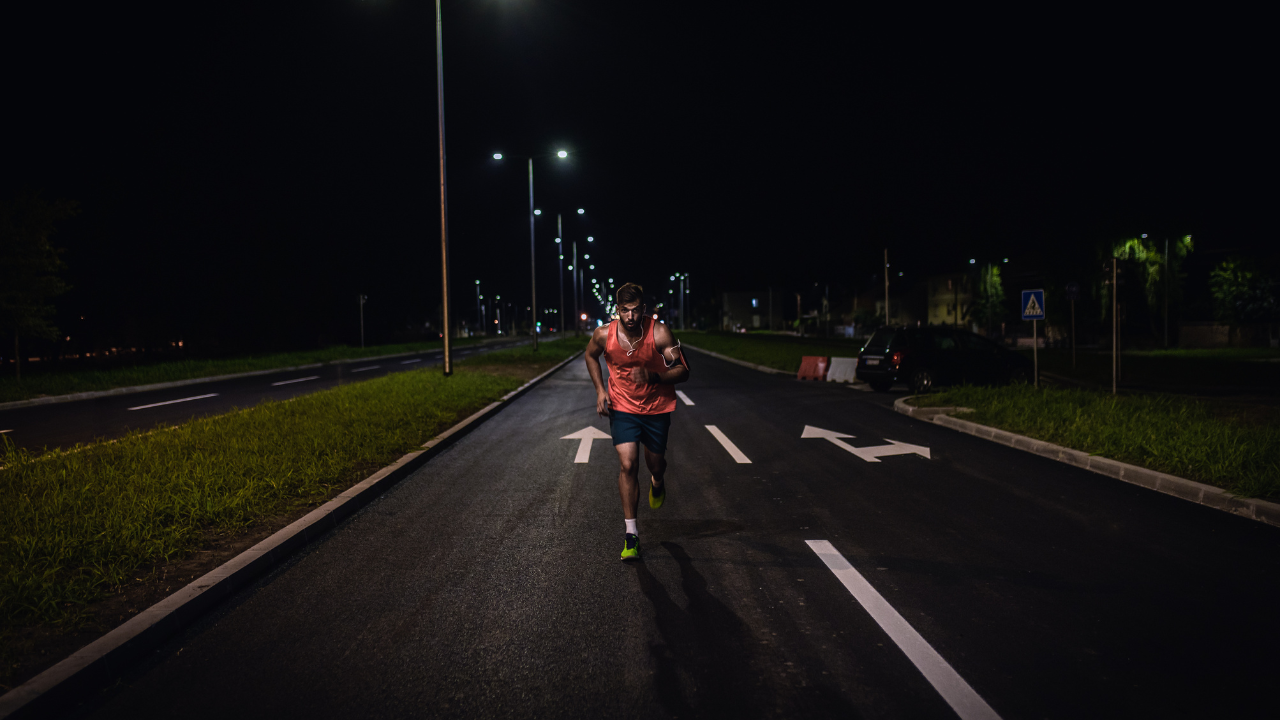 A person in athletic gear runs on a well-lit, empty street at night, reminiscent of a Wings For Life World Run. The street lights and road markings are clearly visible.