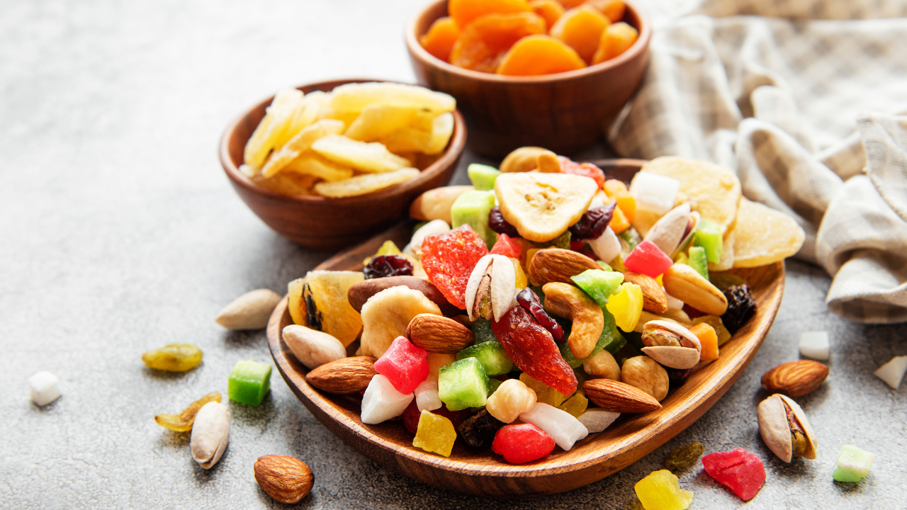 A wooden bowl filled with an assortment of dried fruits and nuts is set on a table, the ultimate guide to post-run nutrition. Smaller bowls containing dried apricots and banana chips provide additional options for a balanced, nutritious snack.